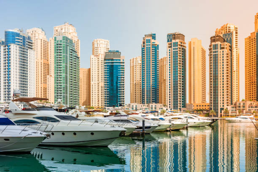 Luxury yachts anchored in a marina with modern skyscrapers in the background near Binghatti Hills.